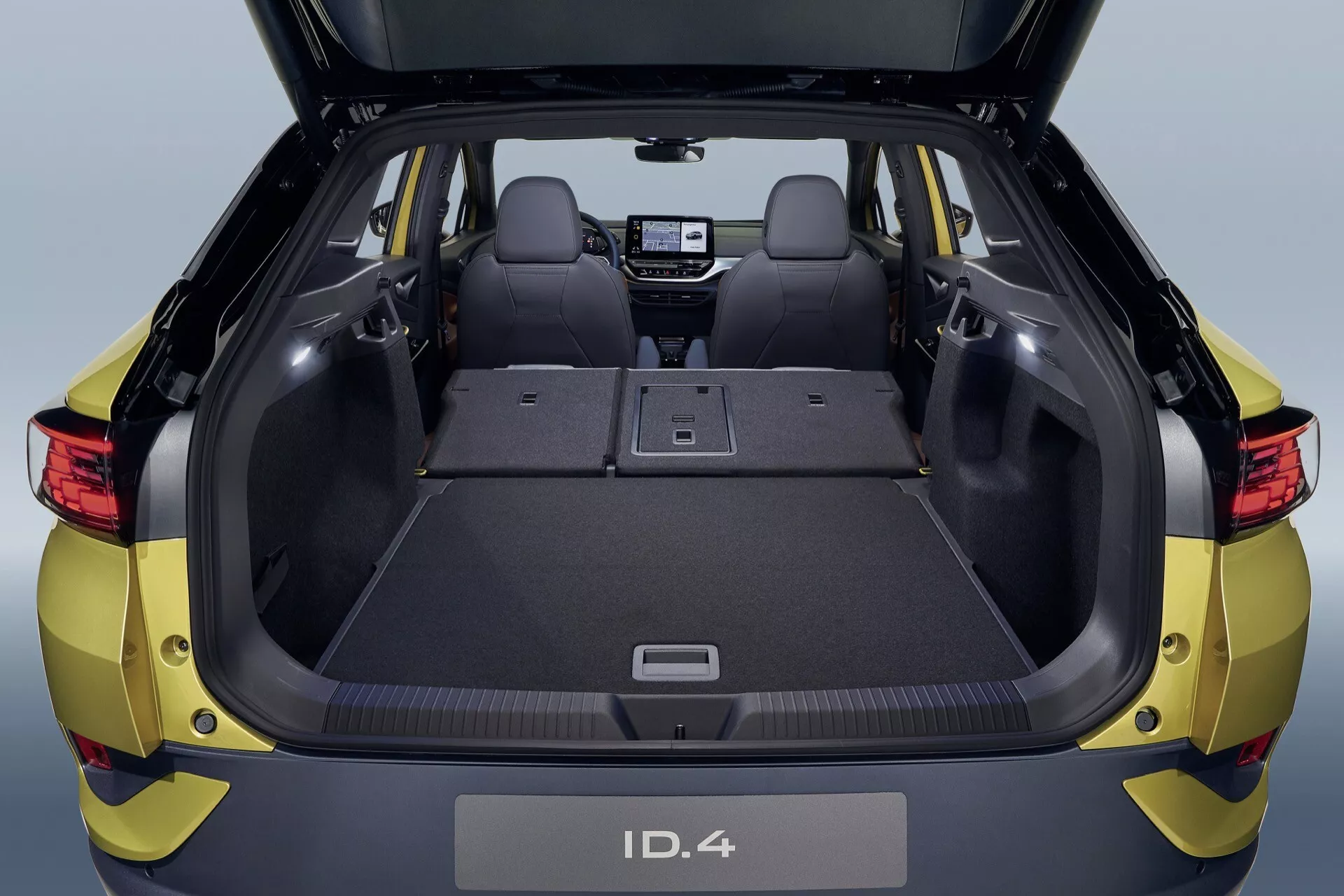 Högvinklad vy av bakre interiören i VW ID.4 1:a generationen 2020 som visar det rymliga lastområdet med bakluckan öppen, nedfällbara baksäten och en modern instrumentbräda med digital display
