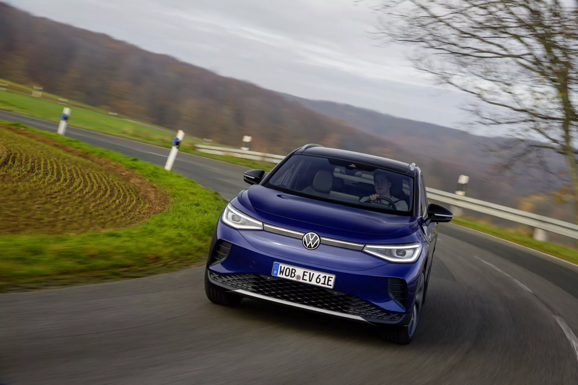 VW ID.4 1:a generationen 2020 i rörelse på landsväg, visar vänster frånvinkel med LED-strålkastare, stängd frontgrill och designelement för elbilar under molnigt dagsljus