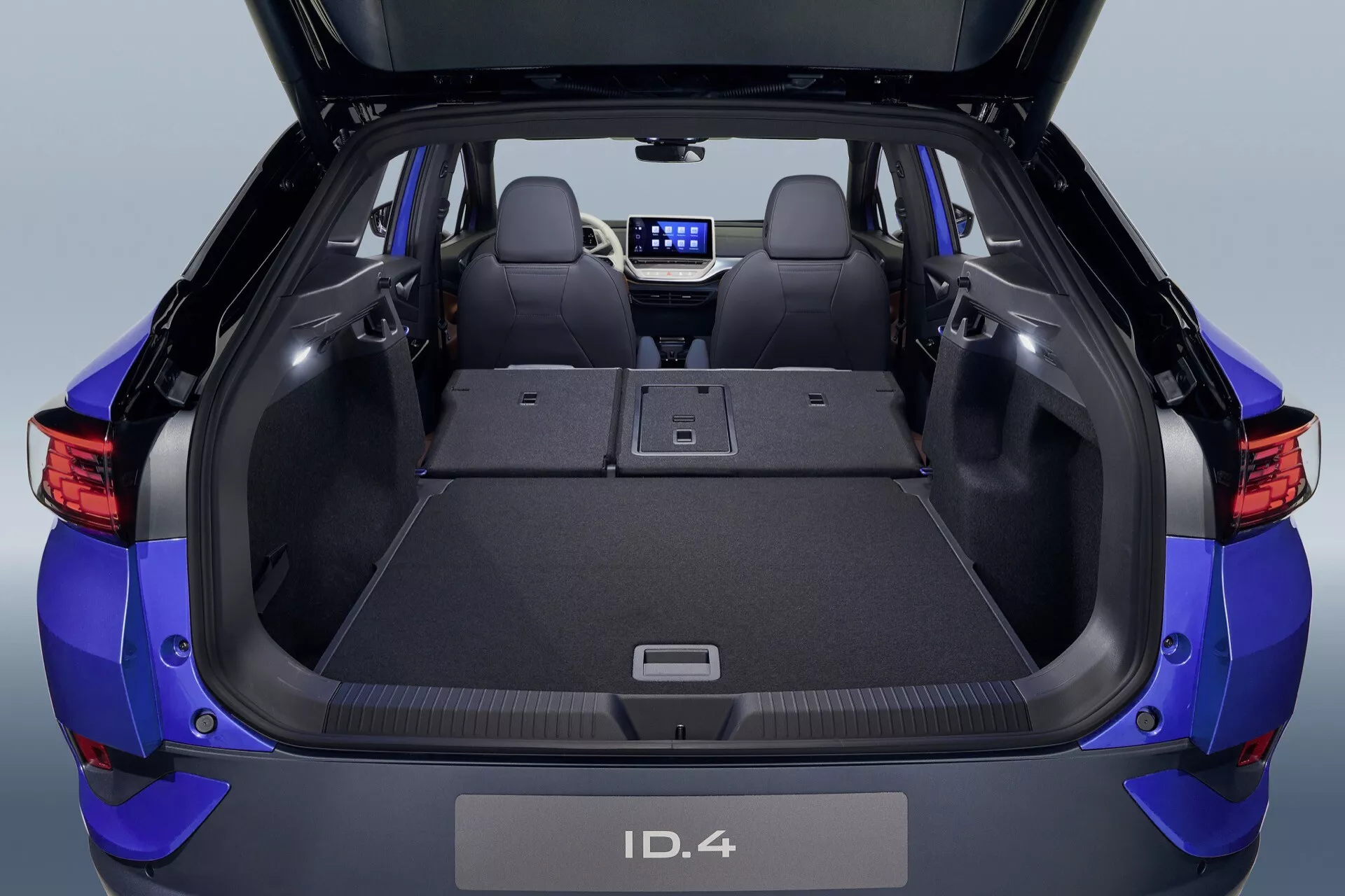 Vy ovanifrån av VW ID.4 2020 bakre interiör och lastutrymme med nedfällda säten, som visar den platta utvidgade lastytan, neddragbart lastskydd och moderna designelement inklusive ett 12V-uttag och genomlastningsfunktionalitet för långa föremål.
