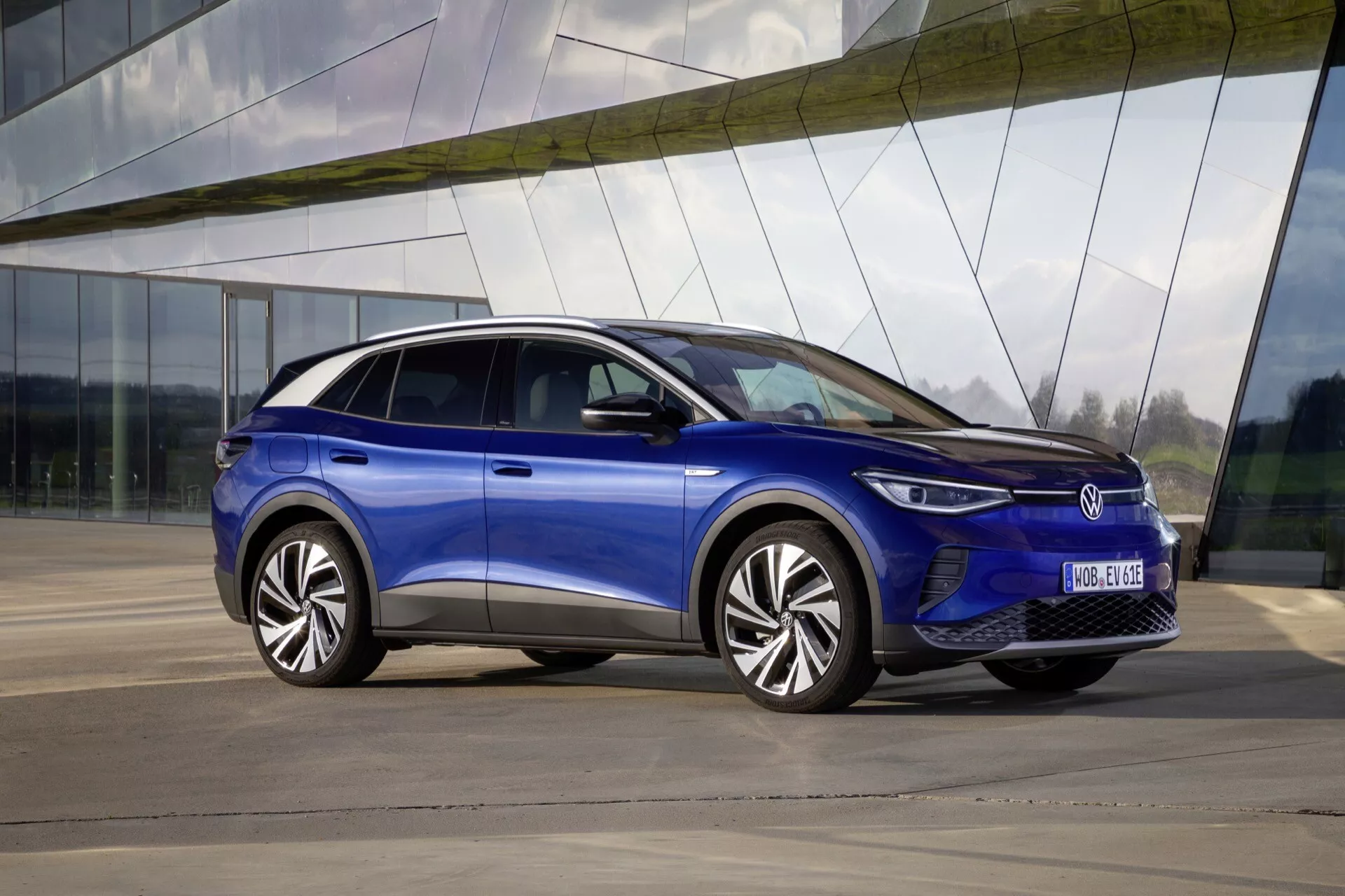 VW ID.4 1:a generationen år 2020 i metalliskt blått parkerad utomhus med en slank design med sluttande taklinje, LED-strålkastare och flerspekiga legeringshjul, mot en modern byggnadsbakgrund
