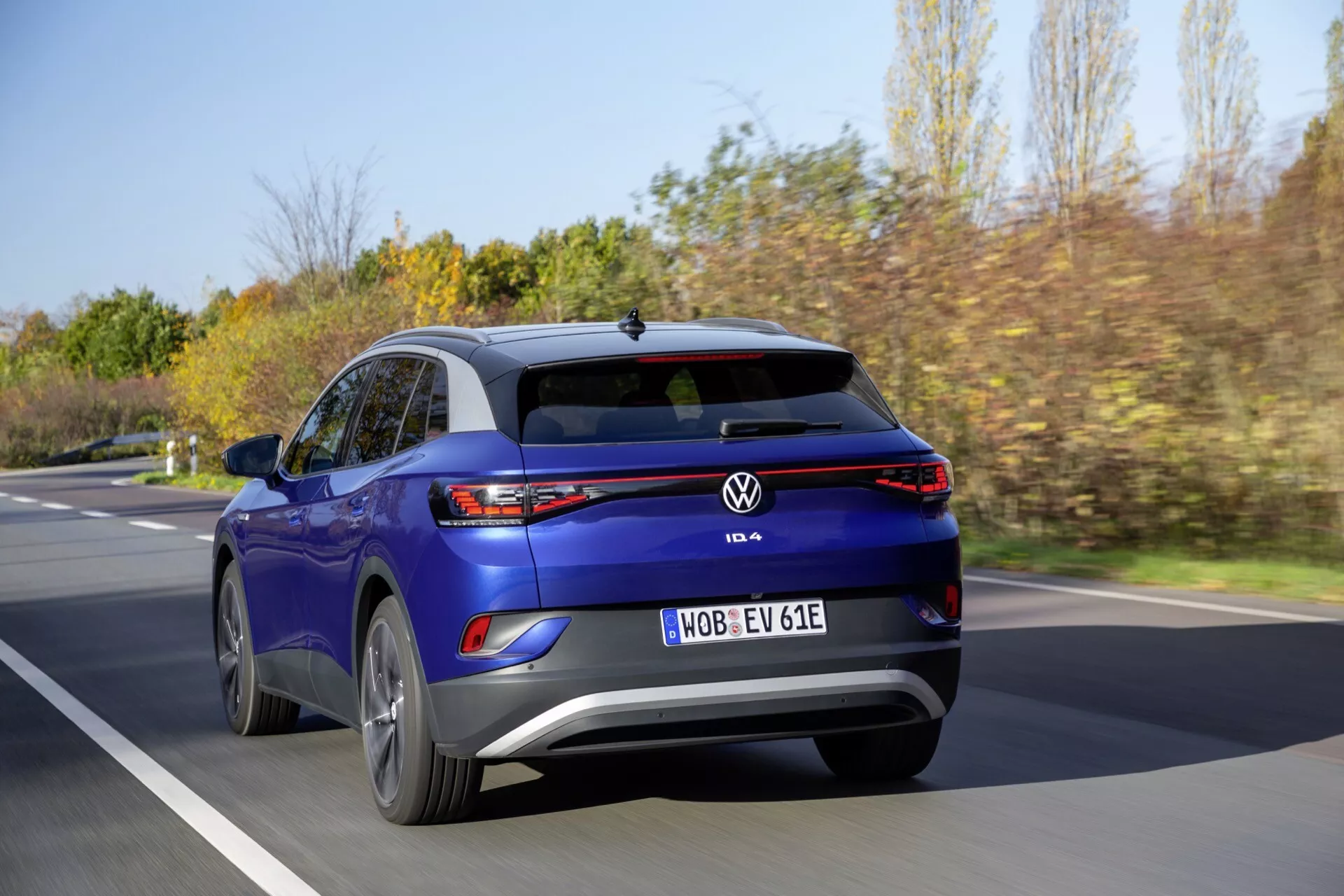 Bakifrån perspektiv av en blå Volkswagen ID.4 elektrisk SUV i rörelse på en suddig vägbakgrund, framhäver distinkta bakljus, bakre stötfångare, baklucka med VW-emblem, och dynamisk ställning