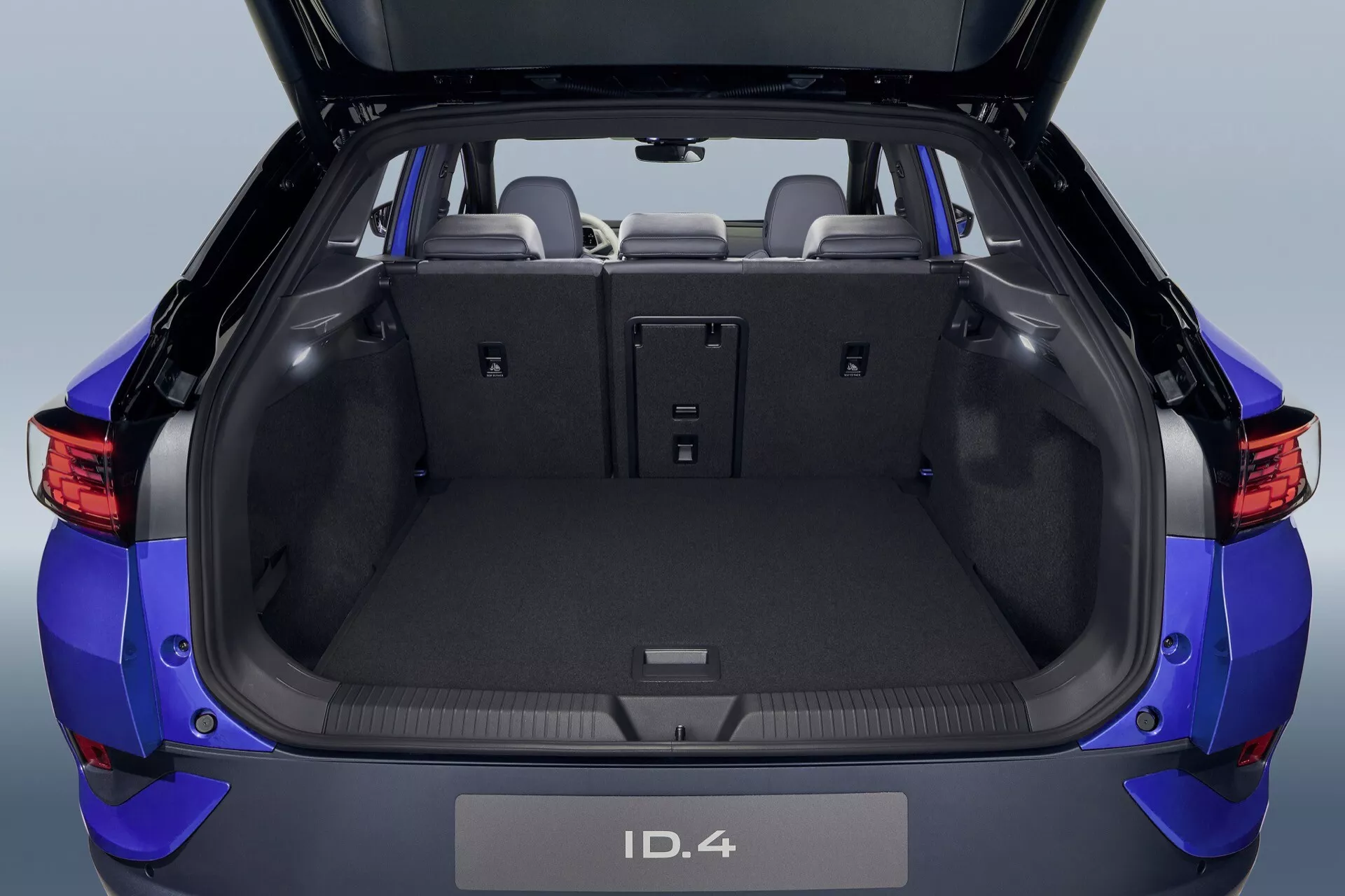 VW ID.4 2020 1:a generationen: modern blå elektrisk SUV bakifrån visar öppen lastlucka med rymlig och flexibel interiör, nedfällda baksäten, bagageutrymme med mattklädsel och avancerad parkeringssensorsteknik.