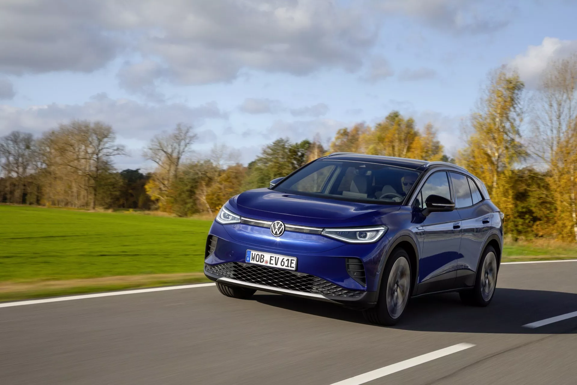Dynamisk bild av en blå 2020 Volkswagen ID.4 elektrisk SUV i rörelse under klara himlar, som visar dess slanka design, LED-strålkastare och aerodynamiska funktioner från ett lågt vinkel, trekvarts utsikt från bilens främre vänstra sida.
