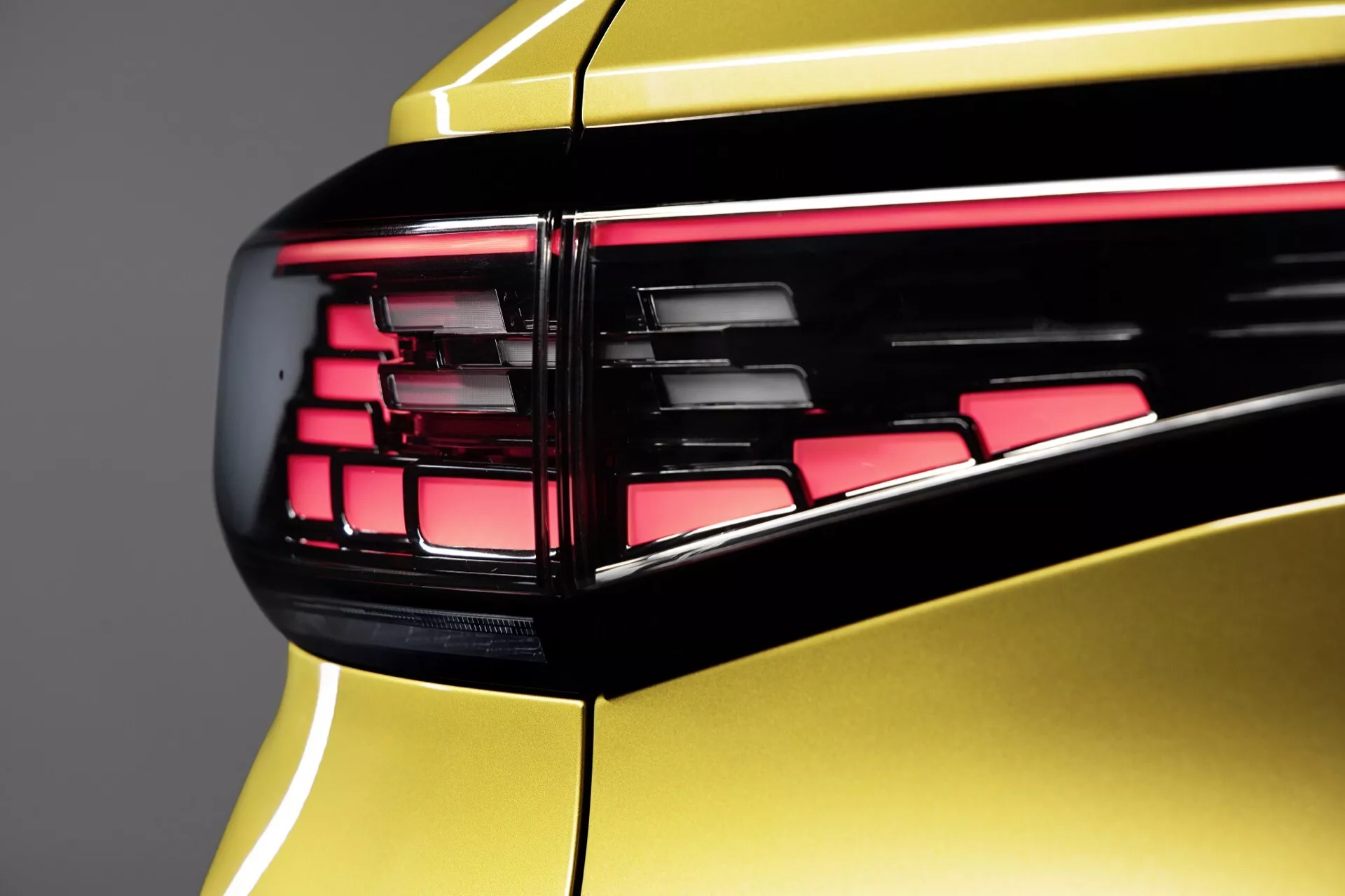 Detaljerad närbild av bakre hörnet på VW ID.4 2020, som visar LED-bakljusenhet med horisontella segment i livlig röd, mot en högglansig metallisk gul kaross-panel, framhäver avancerad ljusdesign och lyxbilens estetik.