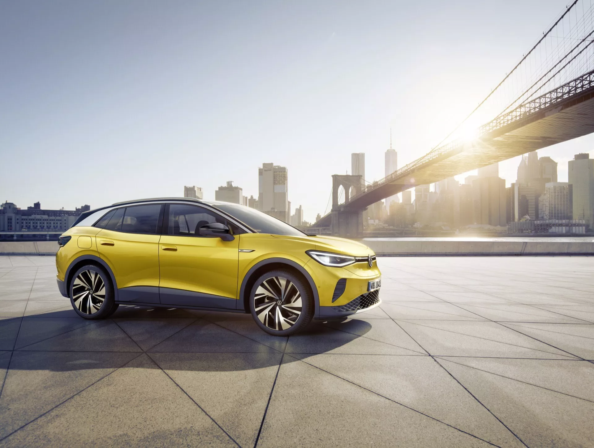 2020 VW ID.4 1:a generationens hatchback/sedan i ljusgul under gyllene timmens ljus, som visar fram- och sidoprofiler med LED-strålkastare och flerspåriga lättmetallhjul, i en urban miljö med brobakgrund