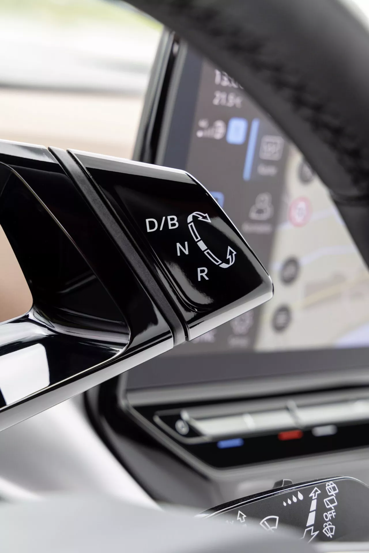 Närbild av interiören i en VW ID.4 2020 som fokuserar på den moderna växelspaken med glänsande svart finish och vit text för Drive, Brake/Battery, Neutral, Reverse och en pekskärms panel i bakgrunden