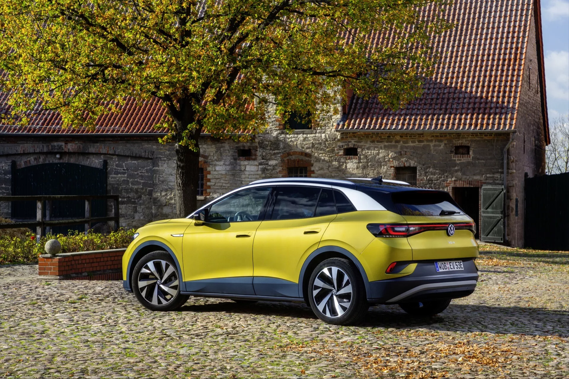 Trekvarts bakåtsikt av limegul VW ID.4 1:a generationens crossover SUV parkerad utomhus, som visar sidoprofil, bakända, aerodynamisk design, LED-bakljus och flerstråliga legeringshjul
