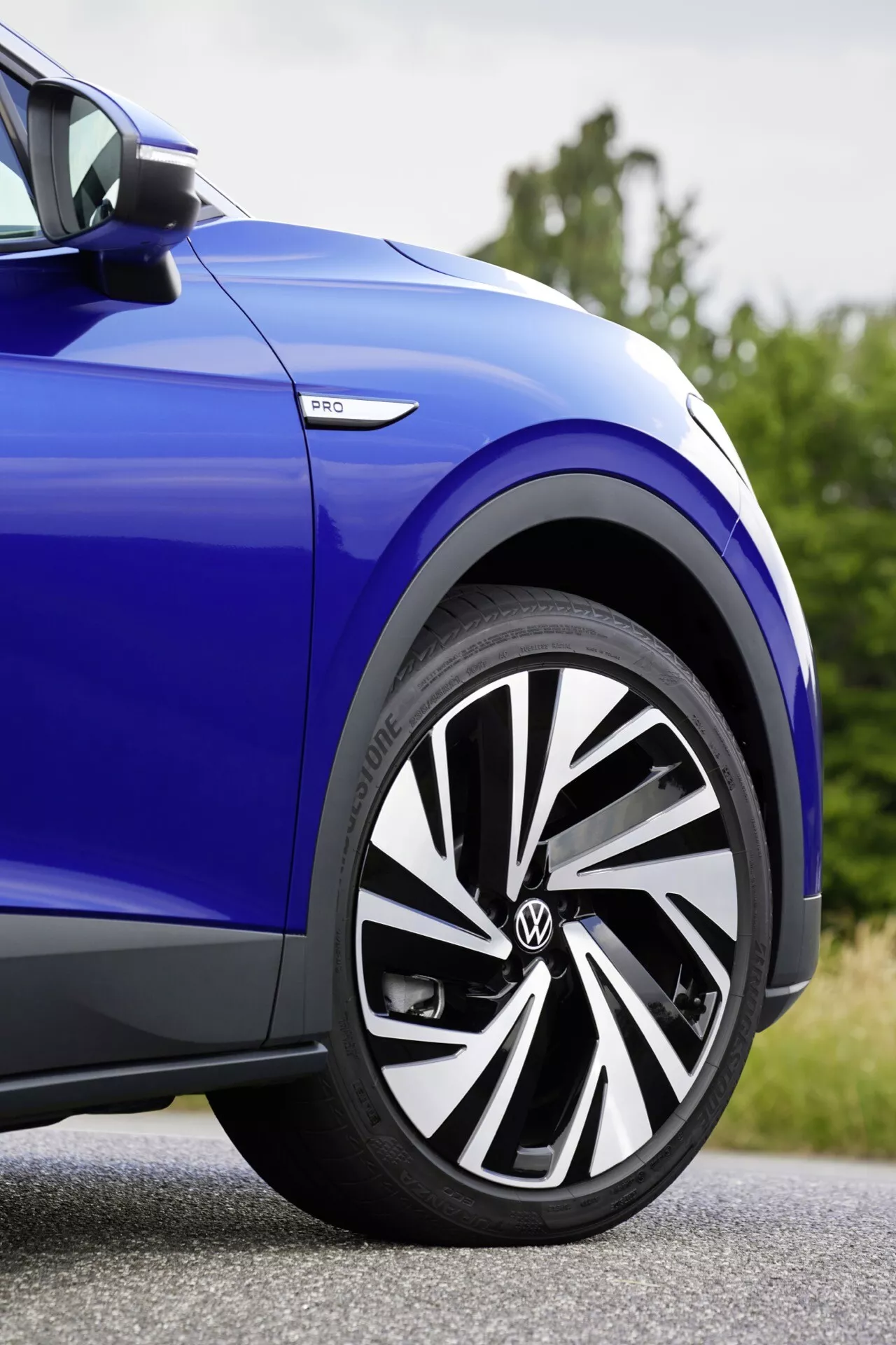 Närbild på sidan av en blå VW ID.4 från 2020, visar framhjulet med en modern legeringsfälg design, Bridgestone däck och eHybrid emblem, betonar dess sportiga utseende och hybridteknik.