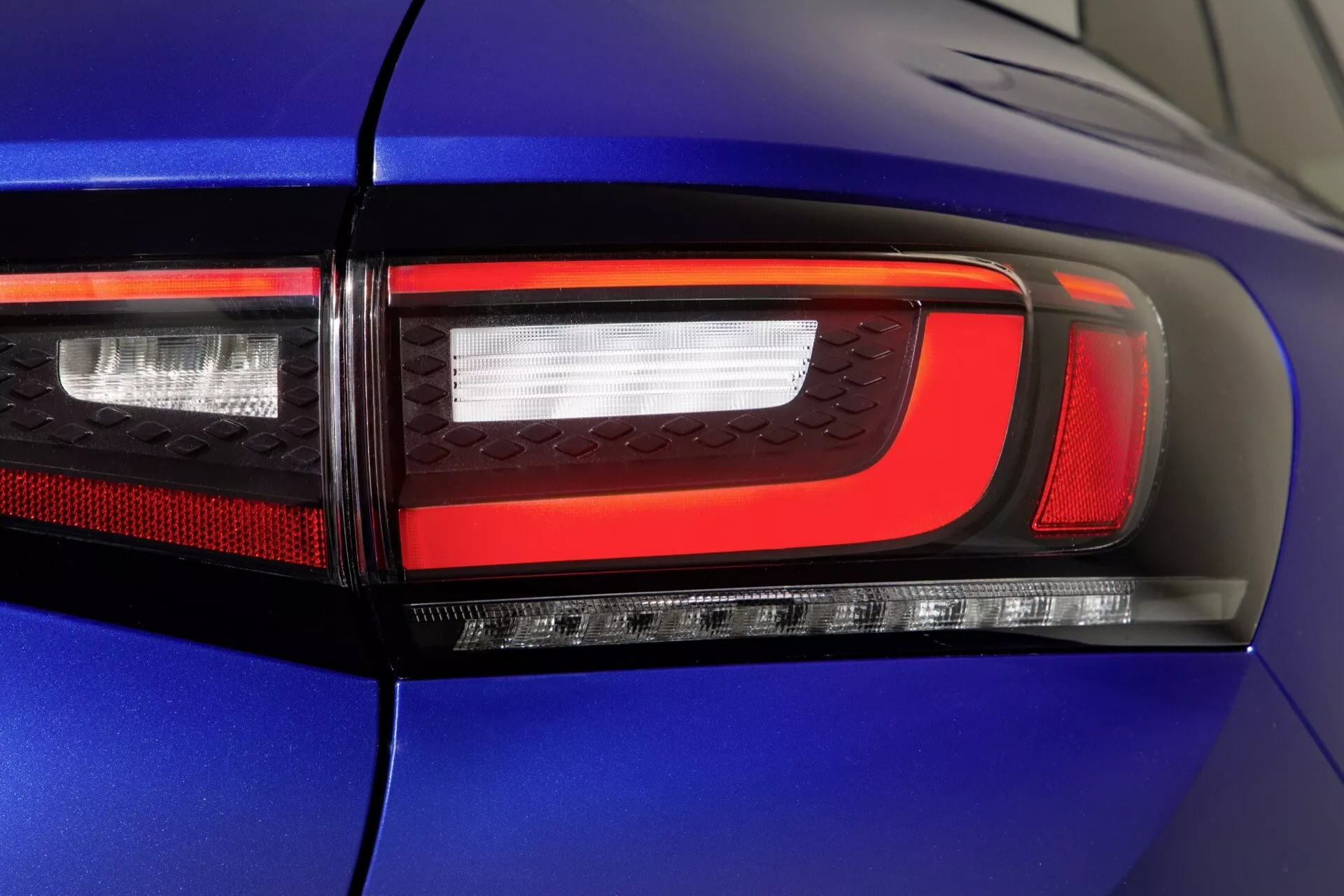 Närbild av den höger sida bakljusmonteringen på en blå VW ID.4 2020 som visar modern LED-teknologi, inklusive bromsljus, blinkers, backljus och eventuellt dimljus sektioner med livliga röda och klara sektioner mot en blank bilkropp.