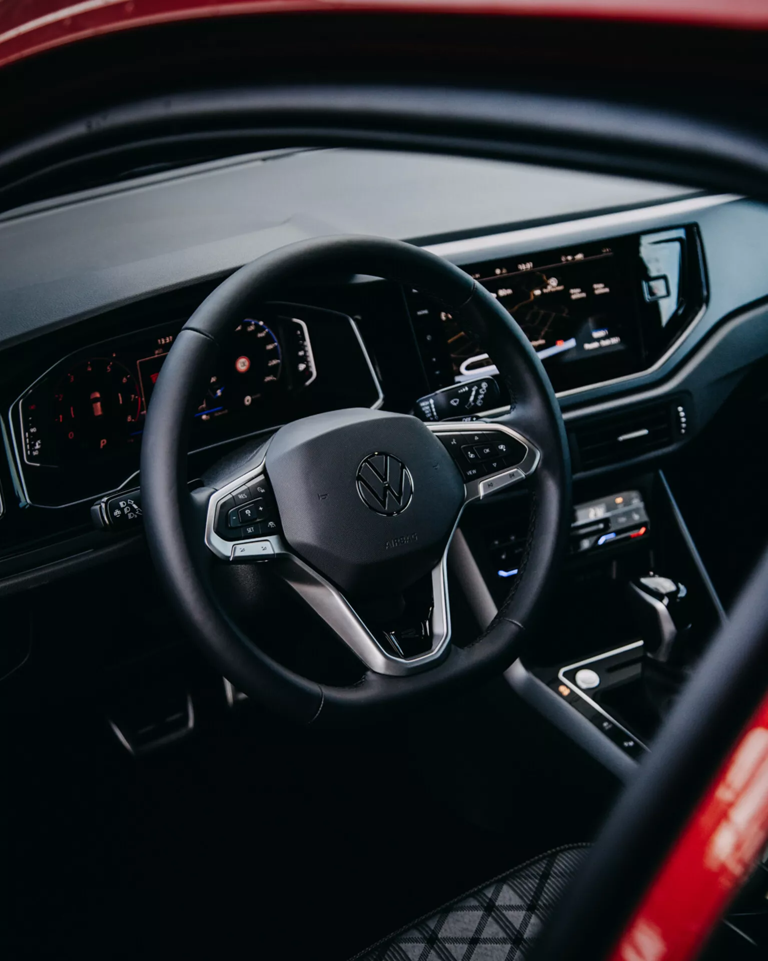 Interiörvy av Volkswagen Taigo 2021 som framhäver ratten med kontroller, digital instrumentbräda och central infotainmentskonsol från en bakre passagerares perspektiv